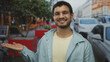 © Krakenimages.com - Young hispanic man with open palm gesture on bustling city street with parked cars and red planters; optimism.