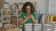 © Krakenimages.com - Middle-aged hispanic woman volunteer in green uniform working in charity indoor room surrounded by donation boxes and meal trays, showing appreciation.