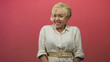 © Krakenimages.com - Senior woman smiling, hands resting on belt, tilting head with earring visible in pink studio; joy.