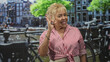 © Krakenimages.com - Woman senior hispanic making ok sign with hand and smiling on street by canal and bicycles, wearing red striped blouse and bracelets; joy.
