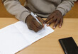 © Tereza - An African-American student in a university classroom is writing in a notebook with a pen