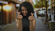 © Krakenimages.com - Woman smiling in urban street showing heart gesture with fingers, indicating joy and connection in a vibrant outdoor setting.