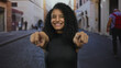 © Krakenimages.com - Woman with curly hair pointing fingers playfully on a city street during daylight, capturing a joyful expression, embodying urban vibrancy and lively interaction.