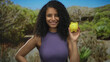 © Krakenimages.com - Hispanic woman smiling outdoors in a park holding a yellow piggy bank, showcasing personal finance and savings in a green natural environment under a clear blue sky