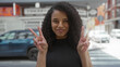 © Krakenimages.com - Woman smiling while making peace signs on a busy city street, exuding joy and positivity under bright daylight with urban surroundings and parked cars in the background.