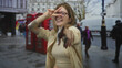 © Krakenimages.com - Woman with glasses shows hand in peace sign gesture toward camera on city street with red phone booths in background; joy.