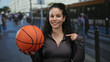 © Krakenimages.com - Woman holding basketball confidently on bustling urban street with people in background capturing dynamic outdoor environment and sporty vibe.