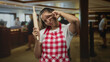 © Krakenimages.com - Woman cook wearing red checkered apron holding a rolling pin and makes v sign to eye in hotel building; playful.