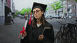 © Krakenimages.com - Woman in graduation gown holds diploma and book on street, face puckered in playful kissy pose; pride achievement celebration.