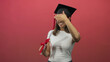 © Krakenimages.com - Woman wearing mortarboard cap and glasses holding diploma scroll with red ribbon, smiling while hand covers eyes in studio; pride celebration.
