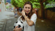 © Krakenimages.com - Young woman holding soccer ball looks emotional on city street during the day, showcasing casual style and tattoo art.