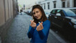 © Krakenimages.com - Young woman in blue sweater making heart symbols with fingers on a city street with parked cars.