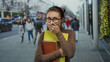 © Krakenimages.com - Woman holding books and covering face stands on bustling city street, wearing glasses and hair tie, suggesting thoughtfulness in urban environment.