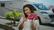 © Krakenimages.com - Woman smiling outdoors holding flowers and pointing finger beside a camper on a sunny city street.