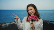 © Krakenimages.com - Woman smiling holding flowers and pointing at the beach with the ocean in the background on a sunny day suggesting relaxation and enjoyment outdoors by the seaside.