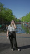 © Krakenimages.com - Woman standing by amsterdam canal outdoors in spring, surrounded by bikes, wearing sunglasses and casual clothes, enjoying the bright day under a clear blue sky.
