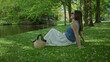 © Krakenimages.com - Woman relaxing on lush green grass in a serene garden wearing sunglasses with a woven handbag nearby under shaded trees by a serene pond in summer.
