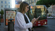 © Krakenimages.com - Young woman texting on smartphone with hands, wearing glasses and a white shirt on a rome street while looking at screen; urban concentration.