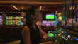 © Krakenimages.com - Young woman pressing slot machine buttons at a row of machines in building with a drink on the console; night fun anticipation.