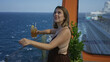 © Krakenimages.com - Woman holding iced drink while leaning on deck railing, smiling and touching hair on cruise ship deck; vacation relaxation.