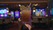 © Krakenimages.com - Woman holding cocktail with lemon slice offers drink to camera inside casino building; playful invitation.