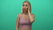 © Krakenimages.com - Woman wearing sports bra touches cheek with hand in studio against green wall; toothache discomfort.