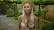 © Krakenimages.com - Blonde woman stands showing bare breasts in green park walkway under straw hat framed by leafy arbor; serenity.