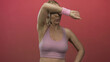 © Krakenimages.com - Woman in a sports bra wipes sweat from her forehead with her elbow in a bright pink studio; determination.