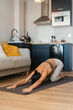 © sutulastock - Fit woman stretching in a child’s pose on a yoga mat in a cozy modern apartment, extending her arms forward and lowering her body for relaxation, flexibility, and mindful home practice.