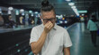 © Krakenimages.com - Man pinched nose with hand over face standing on platform inside train station building, glasses and white polo visible; disgust delay.