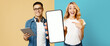 © Prostock-studio - A young man with glasses holds a tablet while a woman points at a blank phone. They both display excitement in a colorful set with yellow and blue backgrounds, showing a trendy atmosphere.