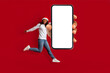 © Prostock-studio - A joyful woman dressed in a festive outfit with a Santa hat jumps playfully while holding a large blank smartphone in front of her. The bright red backdrop enhances the cheerful atmosphere.