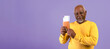 © Prostock-studio - A man stands in front of a purple background holding a wallet with cards. He has a smile on his face and appears confident and at ease. The setting highlights his casual attire.