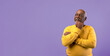 © Prostock-studio - A man stands confidently with his arms crossed and a thoughtful expression. He is looking slightly upward and is dressed in a yellow sweater with a purple background.