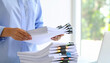 © AucArtStudio - Clutter paperwork office desk massy chaos overload stress work busy woman holding stacked document with binder clips bright workspace showing