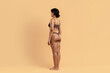 © Anastasiya - Side profile of young black woman in brown underwear standing on beige background. Defined waist, toned hips and sculpted glutes reflect weightloss progress and fitness results