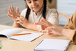 © Pixel-Shot - Mother with her little daughter using sign language while doing homework in kitchen, closeup