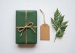 © Turzo Khan - A neatly wrapped gift box in deep green, tied with twine, sits beside a blank gift tag and a sprig of evergreen, perfect for holiday or special occasion