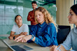 © we.bond.creations - Diverse business professionals working together, discussing ideas and pointing at a laptop screen in a modern corporate meeting room