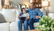 © Jelena Stanojkovic - Tablet, relax and father with child on sofa playing online video game in living room at home. Happy, bonding and dad teaching boy kid esports on digital technology for fun together in lounge at house
