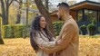 © Yuliia - Hispanic happy couple in love outdoors talking in city fall season man and woman communicate in autumn park guy pointing away discuss talk with girl dating going away windy weather yellow foliage leaf