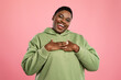 © Prostock-studio - A woman stands with her hands over her chest, smiling brightly while wearing a green hoodie. Her joyful expression contrasts beautifully with the pink background.