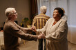 © Seventyfour - Senior Caucasian man and senior Black woman dancing together in nursing home, holding hands and smiling, other seniors standing in background, engaging in social activity