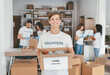 © Prostock-studio - A group of volunteers helps sort and package food donations at a community center. One volunteer smiles while holding a box labeled food donations, showcasing their commitment to helping others.