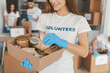© Prostock-studio - A group of volunteers sorts food items at a community center. A woman holds a box filled with various canned goods and dried food while wearing blue gloves.