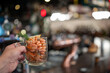 © pavel siamionov - A hand holds a glass mug filled with cooked, shell-on prawns, garnished with a lemon slice and dill, in a dark, atmospheric pub or restaurant setting with bokeh lights