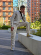 © Pavel Losevsky - Man in a white shirt and tan pants is leaning against a wall. He is wearing a black backpack is surrounded by tall buildings