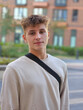 © Pavel Losevsky - Young man wearing a white shirt and black backpack. He is smiling. The background is a brick building