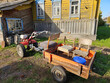 © Pavel Losevsky - Red bike plow ATV is parked next to a trailer. The trailer has a chair and a bucket on it near house