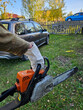 © Pavel Losevsky - Man is holding a chainsaw in a yard. A car is parked behind him. A bicycle is parked in front of the car